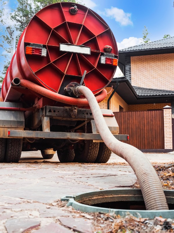 Red Septic Tank Truck With A Hose Connected To An Open Manhole In A Residential